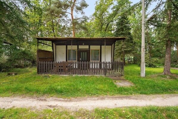 Eine kleine Holzhütte mit einem eingezäunten Veranda, umgeben von Bäumen.