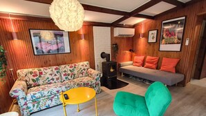A cozy living room with a sofa, a chair, a small table, a fireplace, and wooden walls. - 4 Star Holiday Home in Ry (Ry)