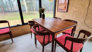 A dining area with a wooden table and red cushioned chairs, large windows with a view of trees, and a hanging light fixture. - 4 Star Holiday Home in Ry (Ry)