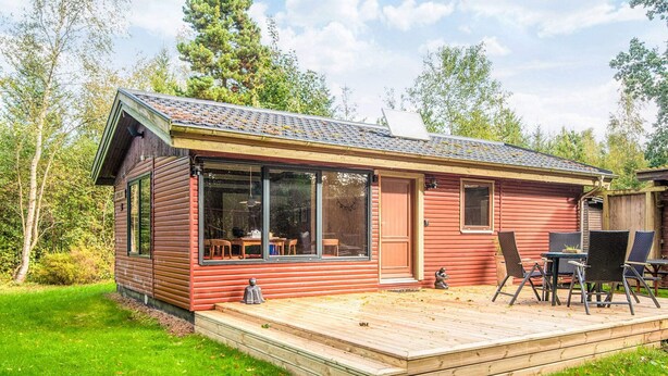 A wooden cabin with a deck, large windows, and a dining area with outdoor furniture. - 4 Star Holiday Home in Ry (Ry)