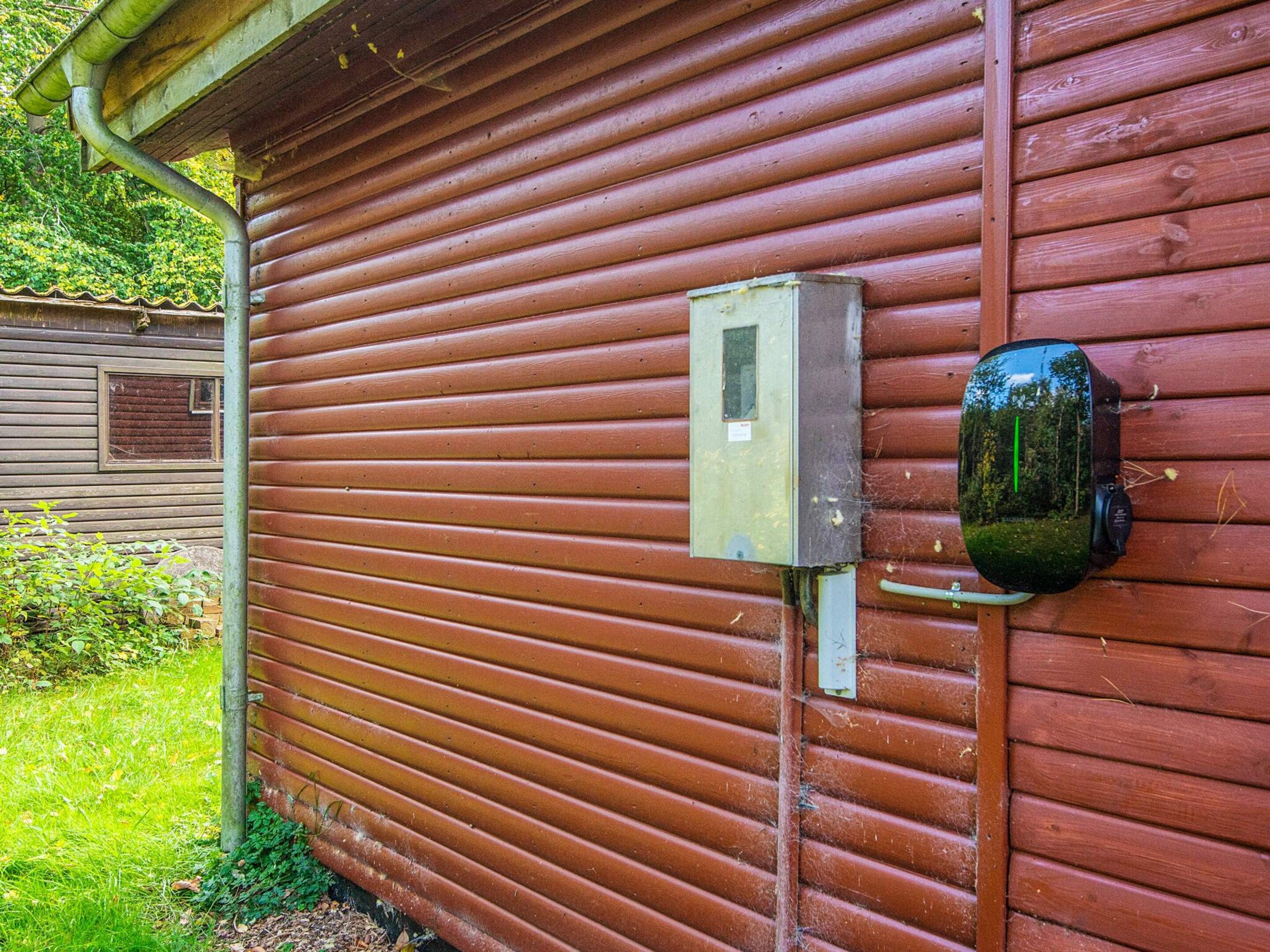 A red wooden building with a metal electrical box and a security camera mounted on the wall.
