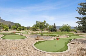 Een midgetgolfbaan met meerdere holes, omgeven door bomen en een bergachtige achtergrond.
