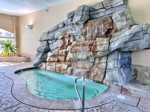 Une piscine avec un mur de roche en arrière-plan, une échelle en métal et un sol carrelé.