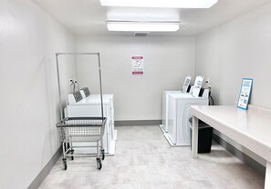 Une buanderie équipée d’un chariot, de machines à laver et d’un panneau affiché sur le mur.