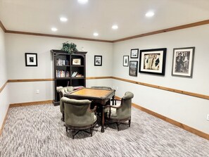 Une pièce comprenant une table de billard, des chaises, une bibliothèque et des tableaux encadrés accrochés aux murs.