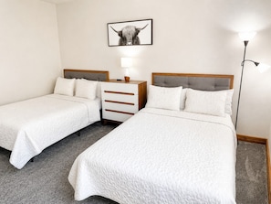 Habitación de hotel con dos camas individuales, una mesita de noche, una lámpara y un cuadro en la pared.