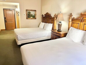 Una habitación de hotel con dos camas, cabecero de madera, lámpara de noche y un cuadro enmarcado en la pared.