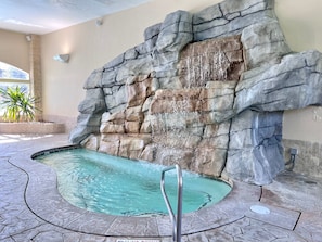 A pool with a waterfall feature, surrounded by stone walls and a tiled floor.