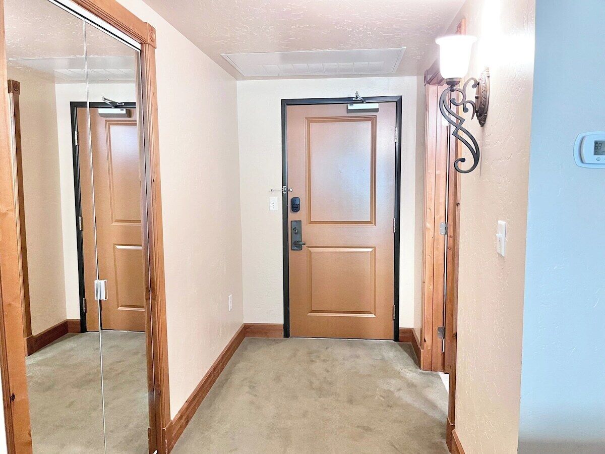 A hallway with a wooden door, a glass door, and a light fixture on the wall.