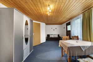 Ein Zimmer mit Holzboden, einem Bett mit kariertem Überwurf, einer Couch, einem Tisch mit Stühlen und einem Kleiderschrank.