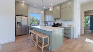 Une cuisine moderne dotée d’un grand îlot central, de tabourets en bois et de meubles de couleur claire.