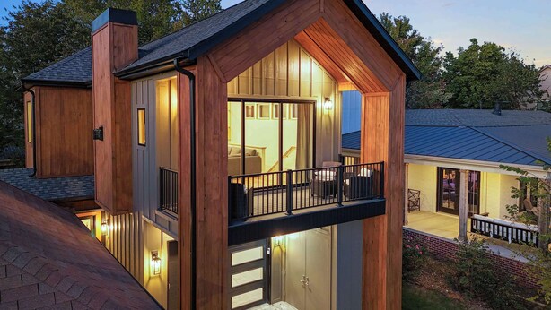 Une maison moderne avec une façade en bois, un balcon et un intérieur visible comprenant un canapé et un coin repas.