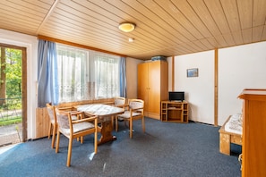 A room with a wooden ceiling, a round table with chairs, a bed, a TV, and a wardrobe.