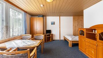 Een kamer met houten plafond, een eettafel met stoelen, een bed, een tv-meubel en een kast.