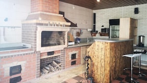 An outdoor kitchen with a brick oven, wooden bar counter, and tiled flooring. - Guest House Discovery (Almaty)
