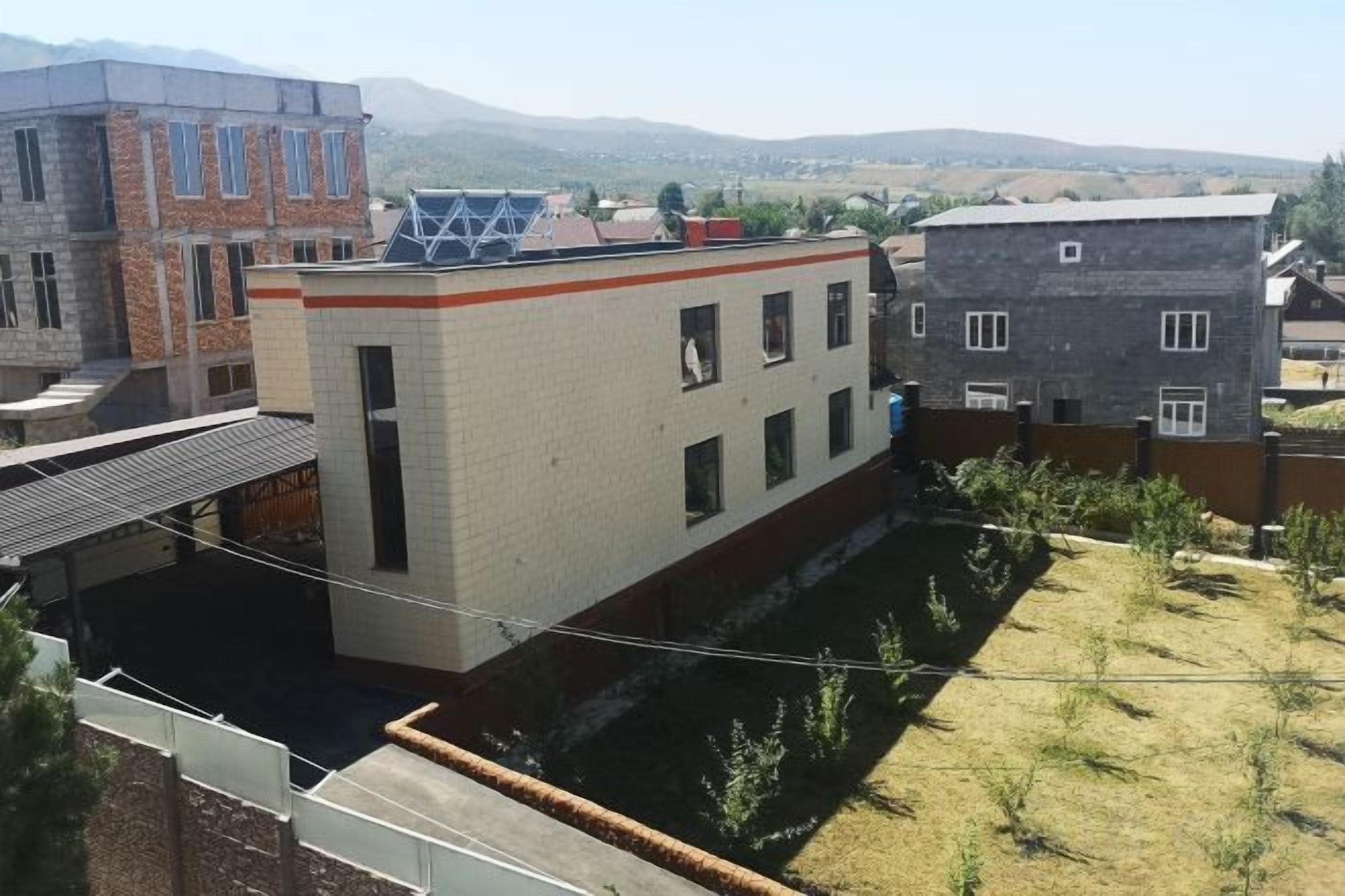 Un immeuble d’habitation doté d’un toit plat, d’une façade en briques et d’une petite cour avec une végétation clairsemée.