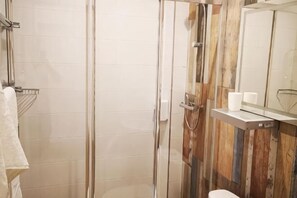 Une salle de bain dotée d’une douche à parois en verre, de toilettes, d’un porte-serviettes et d’un miroir orné d’un panneau en bois.