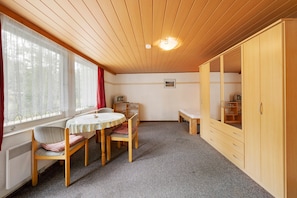 Une pièce avec un plafond en bois, une table ronde entourée de chaises, un banc, une armoire et un radiateur.