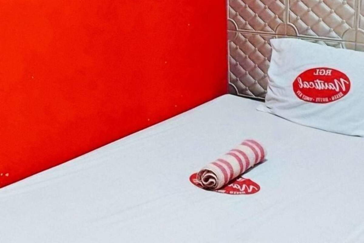 Habitació d'hotel amb una paret vermella, un llit blanc amb un coixí rayat i un coixí amb un logotip vermell.