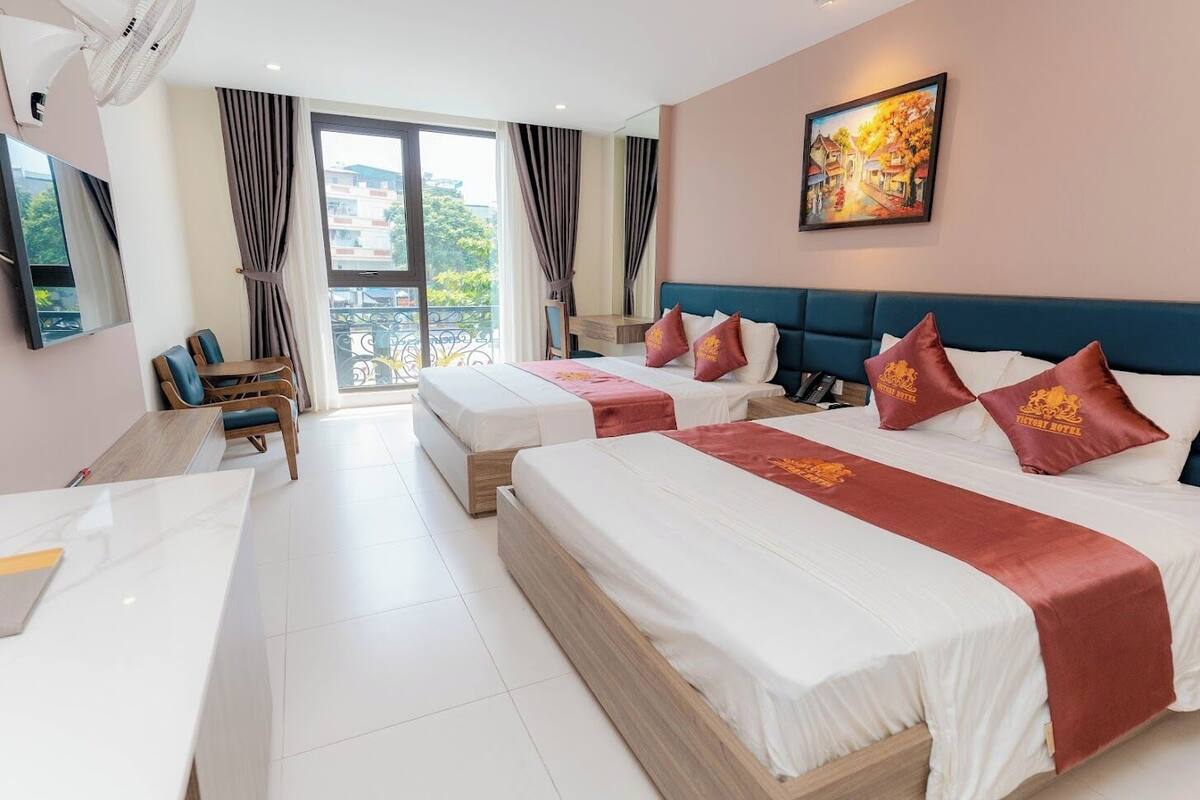 A hotel room with two beds, a desk, a chair, and a balcony with curtains.
