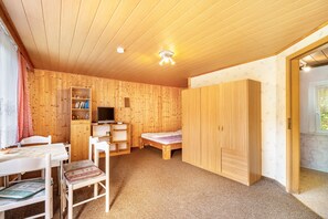 A wooden-paneled room with a bed, a TV, a bookshelf, and a dining area.