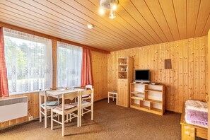 A wooden-paneled room with a table, chairs, a TV, and shelves.