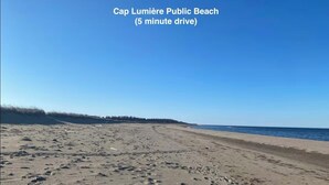 A wide sandy beach with visible footprints, a clear sky, and the ocean in the background.