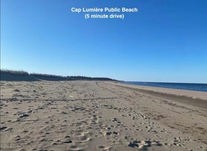 A wide sandy beach with visible footprints, a clear sky, and the ocean in the background.