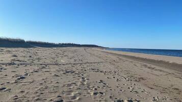 A wide sandy beach with visible footprints, a clear sky, and the ocean in the background.
