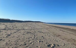 Une vaste plage de sable où l’on peut voir des empreintes, un ciel dégagé et l’océan en toile de fond.