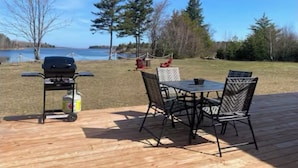 A wooden deck with a grill and chairs, overlooking a lake. - Waterfront tiny home with hot tub (Pet friendly, near beaches) (Richibucto-Village)
