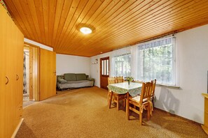 Ein Zimmer mit Holzboden, einem Esstisch mit Stühlen, einer Couch und einem Fenster mit Vorhängen.