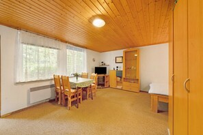 A room with a wooden ceiling, a dining table with chairs, a television, a cabinet, and a bed.
