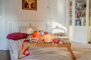 Un lit bien fait, sur lequel on a disposé un plateau d’oranges, une bougie et un cloche de verre recouvrant un plat.