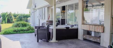 Un patio exterior con área de estar techada, un jacuzzi y una rústica chimenea de ladrillo.