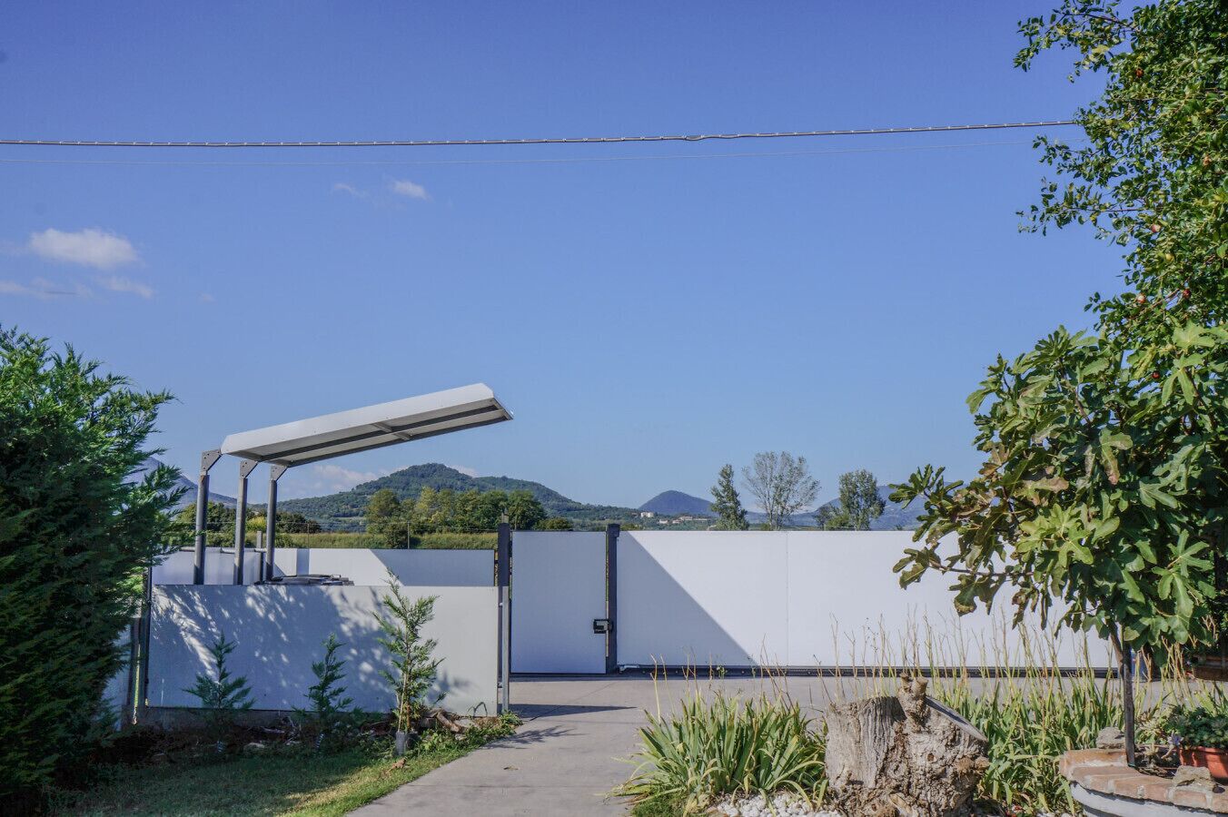 A modern building with a large white wall, a covered walkway, and a view of mountains in the background.