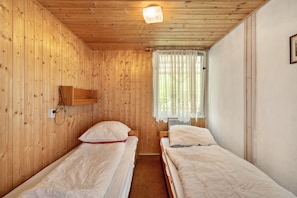 A room with wooden walls, two single beds, a small shelf, and a window with curtains.