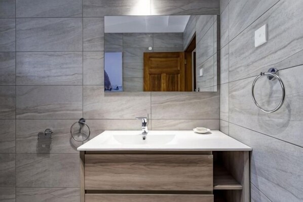 A bathroom with a white sink, wooden vanity, a mirror, and a towel ring. - Lazy Days (Galu)
