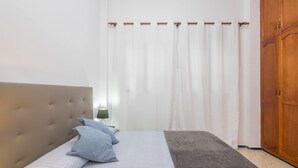 Un dormitorio con cabecera capitonada, cama con ropa de cama a rayas, una manta gris y un armario de madera.
