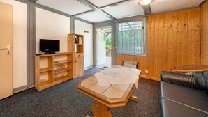 A room with a television, wooden shelves, a table with a placemat, a leather sofa, and a window with a view.