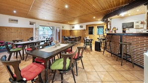 A restaurant with wooden ceiling, multiple tables and chairs, a bar area, and a chalkboard menu.