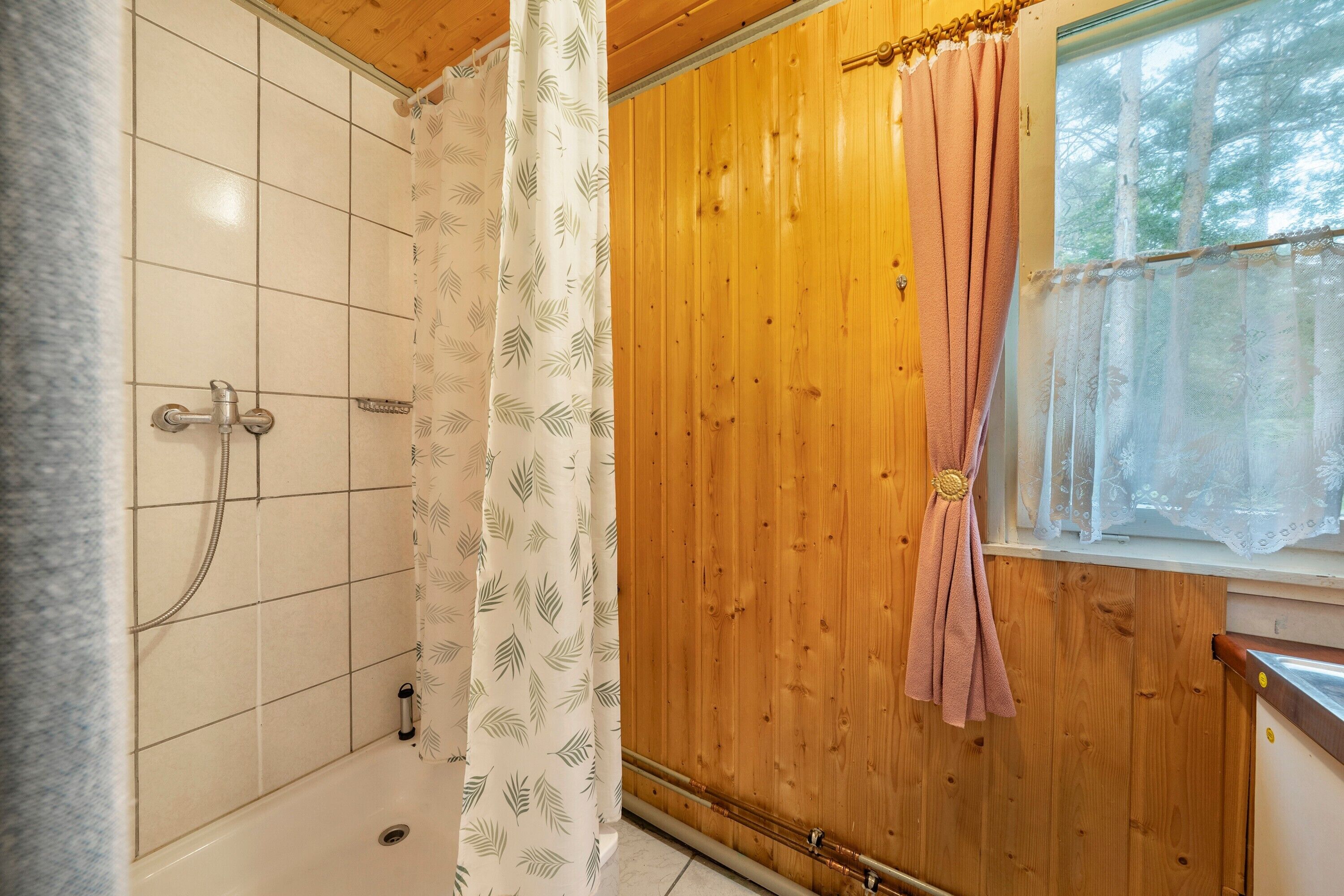 Ein Badezimmer mit Dusche, einer Holzwand und einem Fenster mit Blick auf Bäume.