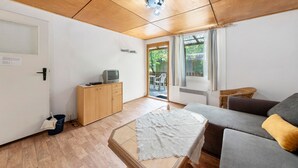 A room with a wooden ceiling, a sofa, a television on a cabinet, and a door leading outside.