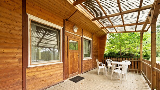 A wooden cabin with a covered porch, a door marked '37', and a table with chairs.
