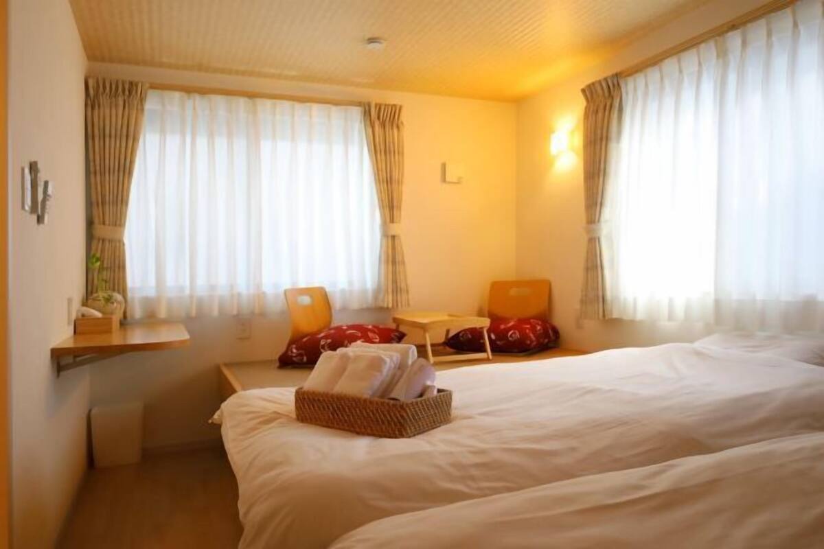Ein Hotelzimmer mit zwei Betten, einem Schreibtisch und einem Stuhl. Auf dem Bett liegt ein Wäschekorb mit Handtüchern und ein kleiner Tisch mit einer Lampe.