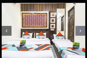 A hotel room with two beds, each with geometric-patterned pillows, a patterned wall hanging, and a wooden door. - PRINCE RESIDENCY (Amritsar)