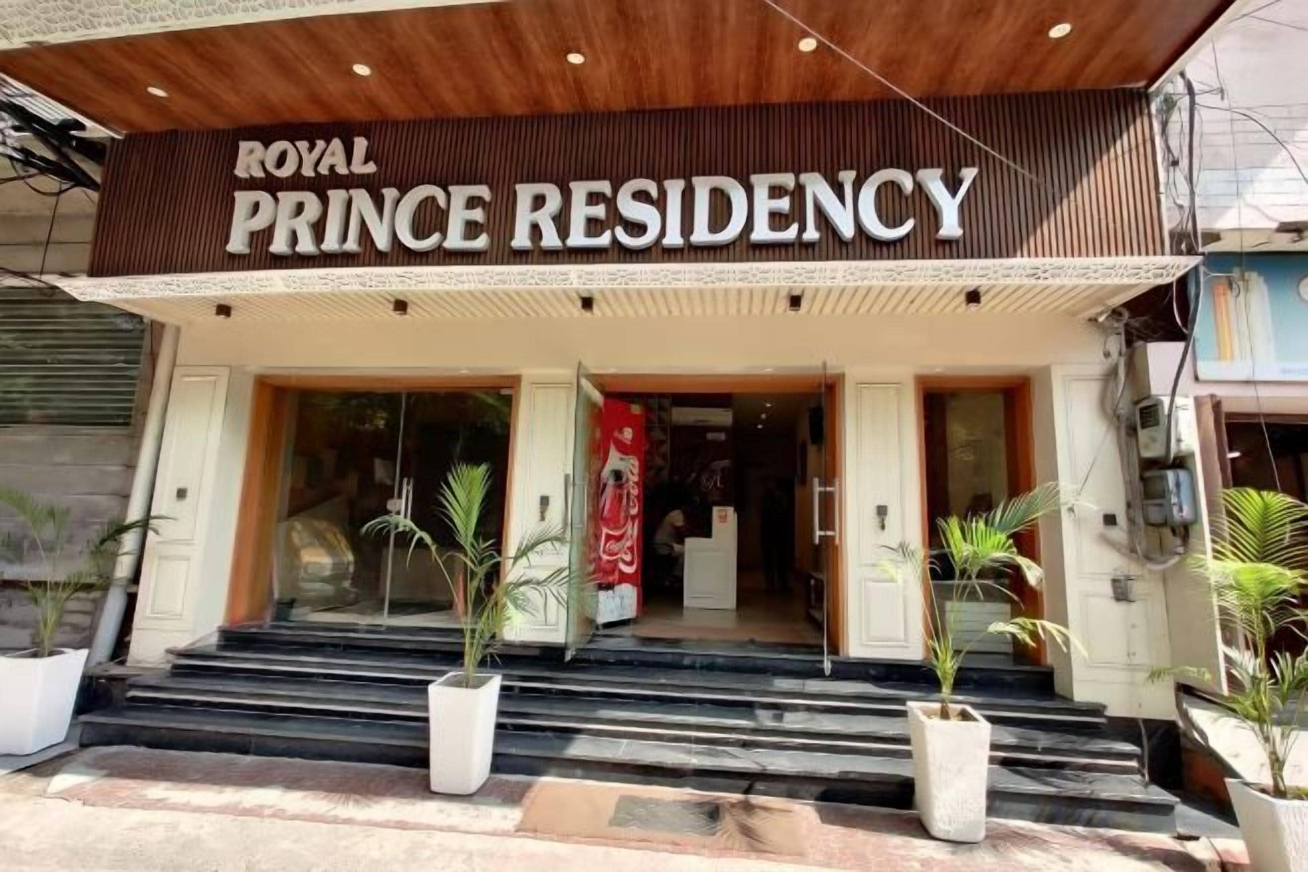 The entrance to the Royal Prince Residency with a sign above the door, a set of steps leading up to the entrance, and potted plants on either side.