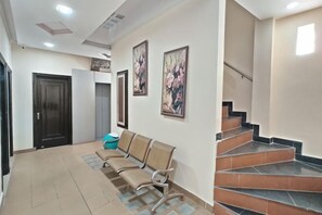 A hotel lobby with a reception desk, a waiting area with chairs, a staircase, and framed artwork on the walls. - PRINCE RESIDENCY (Amritsar)