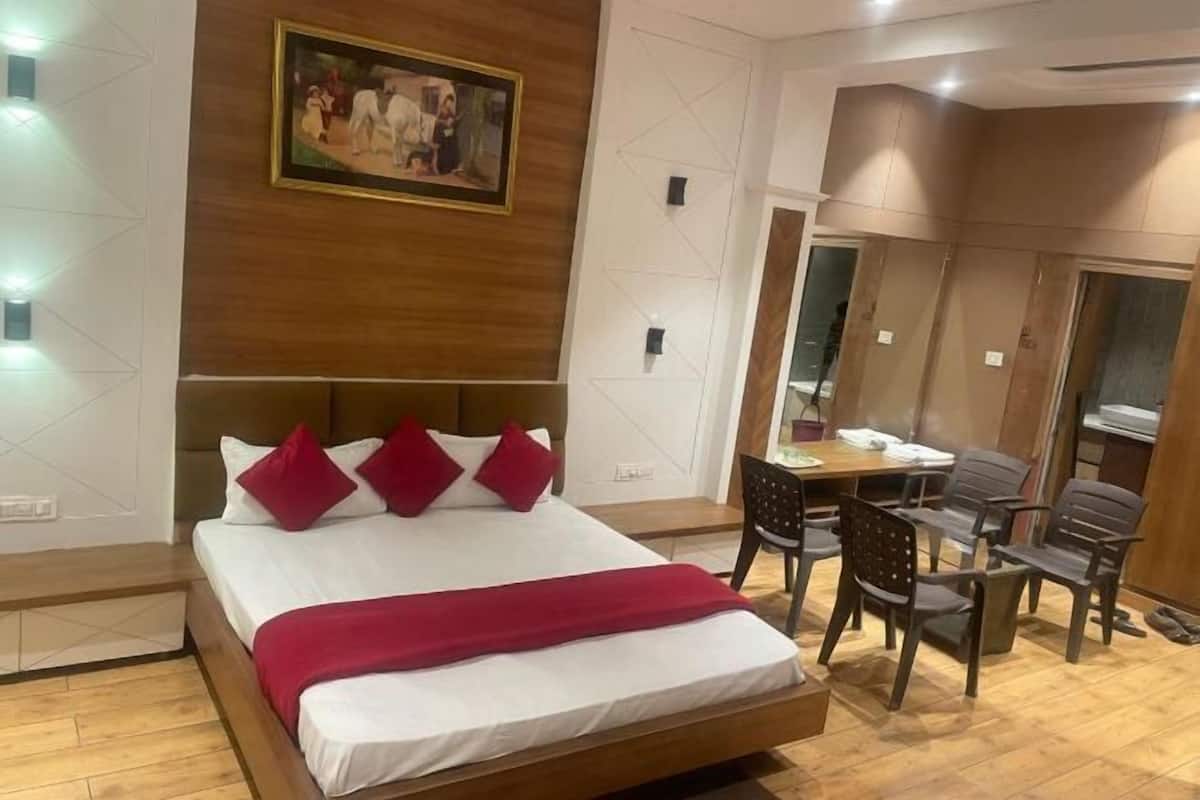 A hotel room with a wooden headboard, a bed with white bedding and red pillows, a desk with chairs, and a mirror.