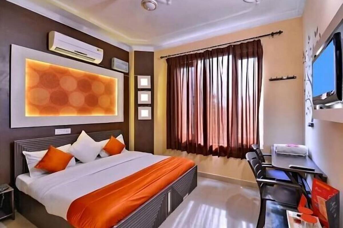 A hotel room with a bed, a desk, a TV, and a large window with curtains.